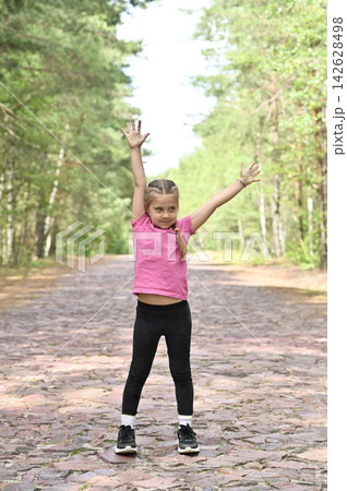 Young girl raises arms on cobblestone forest road, 142628498