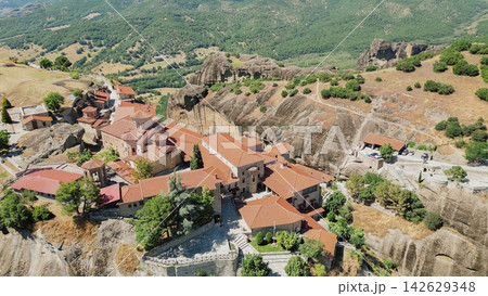Aerial view of Meteora monasteries perched on rocky cliffs surrounded by lush green hills and valleys in Greece, showcasing traditional architecture and natural beauty of the region Aerial view of Meteora monasteries perched on rocky cliffs surrounded by lush green hills and valleys in Greece, showcasing traditional architecture and natural beauty of the region 142629348