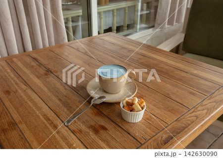 Warm drink with a small bowl of snacks on a wooden table in a cafe during the day Warm drink with a small bowl of snacks on a wooden table in a cafe during the day 142630090