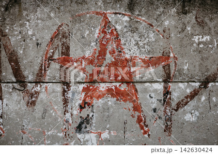 Faded red anarchist graffiti painted on cracked concrete wall with rough texture and urban decay aesthetic. Gritty street art background. 142630424