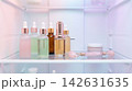 Luxurious cosmetic advertising concept featuring glass dropper bottles and facial tools cooling on a modern refrigerator shelf with soft pastel light 142631635