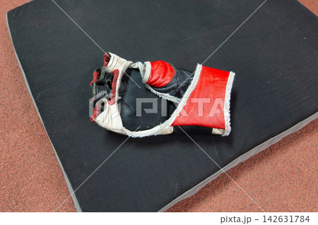 Used boxing glove resting on a black training mat in a gym after a workout session Used boxing glove resting on a black training mat in a gym after a workout session 142631784