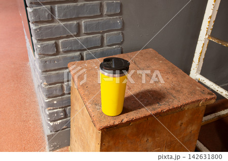 Bright yellow coffee cup on wooden box near gray wall with brick pattern in a casual indoor space Bright yellow coffee cup on wooden box near gray wall with brick pattern in a casual indoor space 142631800