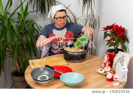 Woman prepares Olivier salad, Russian salad, a traditional Ukrainian or Russian Christmas or New Year dish in a kitchen. She adds boiled green peas to a bowl with other ingredients Woman prepares Olivier salad, Russian salad, a traditional Ukrainian or Russian Christmas or New Year dish in a kitchen. She adds boiled green peas to a bowl with other ingredients 142633530