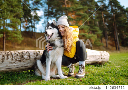 Woman with her husky dog walks in autumn forest. A cheerful pet spends time with its owner outdoors. 142634711
