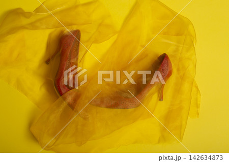 Red women's shoes under sheer fabric on a yellow background Red women's shoes under sheer fabric on a yellow background 142634873