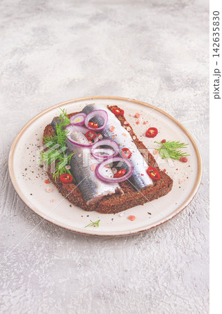 sandwiches , Herring fish, on dark rye bread, sprinkled with onion, chili pepper and herbs, on a light plate sandwiches , Herring fish, on dark rye bread, sprinkled with onion, chili pepper and herbs, on a light plate 142635830