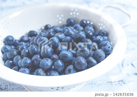 Fresh blueberries in a white colander on a blue surface with water droplets Fresh blueberries in a white colander on a blue surface with water droplets 142635836
