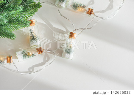 Festive miniature pine trees inside glass bottle string lights on white background with pine branch 142636032