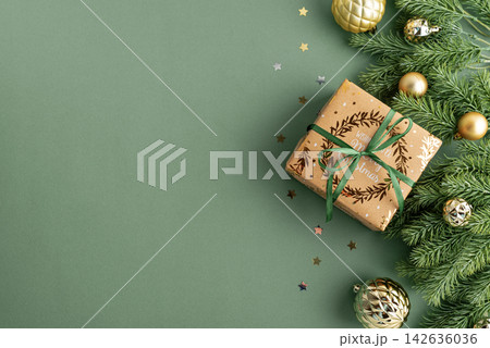 Festive Christmas gift box with ornaments and fir branches arranged on a green background celebrating holiday season joy Festive Christmas gift box with ornaments and fir branches arranged on a green background celebrating holiday season joy 142636036