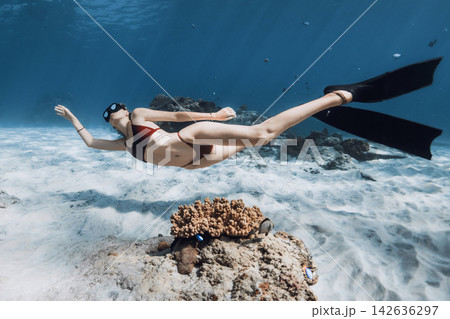 Woman freediver gliding above coral reef and sandy seabed in blue ocean 142636297
