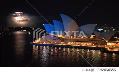 Sydney Opera House iconic architecture illuminates the harbor waters at night, while a dramatic lightning storm flashes in the distant dark sky over the city. Australia main landmark, place to visit Sydney Opera House iconic architecture illuminates the harbor waters at night, while a dramatic lightning storm flashes in the distant dark sky over the city. Australia main landmark, place to visit 142636353