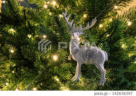 White reindeer ornament on illuminated Christmas tree White reindeer ornament on illuminated Christmas tree 142636397