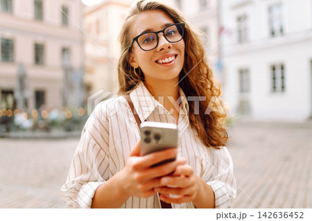 Tourist wearing glasses, holding phone in hands walk around city at sunset. Travel, blogging concept Tourist wearing glasses, holding phone in hands walk around city at sunset. Travel, blogging concept 142636452