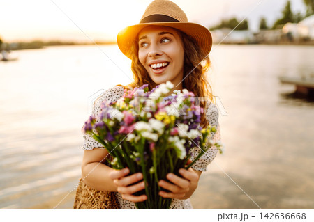 Happy woman in dress sitting on wooden pier near pond and clutched bouquet. Rustic style of wedding. 142636668