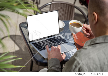Man working on laptop and drinking coffee at outdoor cafe 142637110