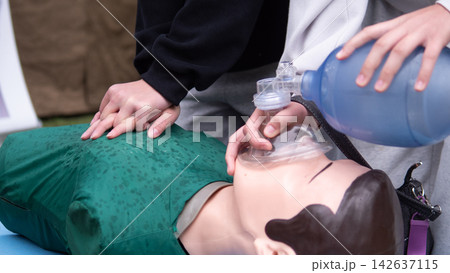 Close view of hands practicing cardiopulmonary resuscitation on training mannequin, fitting rescue breathing mask and squeezing ventilation bag for emergency medical education and teamwork Close view of hands practicing cardiopulmonary resuscitation on training mannequin, fitting rescue breathing mask and squeezing ventilation bag for emergency medical education and teamwork 142637115