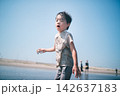 泥だらけで貝殻を拾い振り向く男の子と夏の干潟 142637183