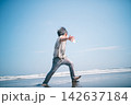 夏の海辺の波打ち際で貝殻を投げて遊ぶ裸足の男の子 142637184