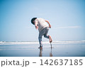 夏の海辺の波打ち際で裸足になり片足を上げて遊ぶ少年 142637185