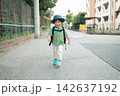 帽子とリュックで住宅街の道を笑顔で歩く男の子 142637192