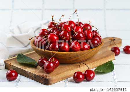 Fresh ripe sweet cherry in wooden bowl on rustic cutting board with green leaves on white background 142637311