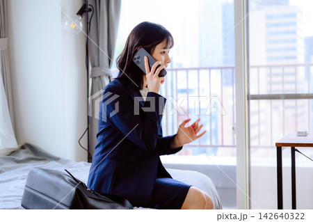 スーツ姿の女性が部屋で電話で話す スマートフォンで通話をしている スーツ姿の女性が部屋で電話で話す スマートフォンで通話をしている 142640322