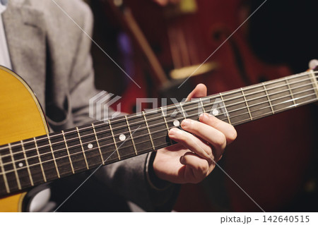 Concert view of acoustic electric guitar player with vocalist and rock band performing in a club, male musician guitarist on stage with audience in a crowded concert club hall arena, hands on guitar 142640515