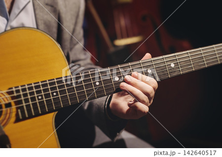 Concert view of acoustic electric guitar player with vocalist and rock band performing in a club, male musician guitarist on stage with audience in a crowded concert club hall arena, hands on guitar 142640517
