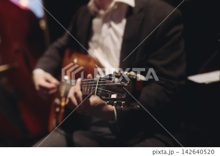 Concert view of acoustic electric guitar player with vocalist and rock band performing in a club, male musician guitarist on stage with audience in a crowded concert club hall arena, hands on guitar 142640520