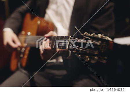 Concert view of acoustic electric guitar player with vocalist and rock band performing in a club, male musician guitarist on stage with audience in a crowded concert club hall arena, hands on guitar 142640524