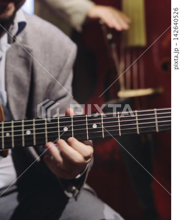 Concert view of acoustic electric guitar player with vocalist and rock band performing in a club, male musician guitarist on stage with audience in a crowded concert club hall arena, hands on guitar 142640526