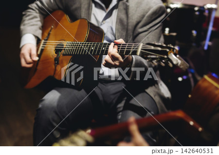 Concert view of acoustic electric guitar player with vocalist and rock band performing in a club, male musician guitarist on stage with audience in a crowded concert club hall arena, hands on guitar Concert view of acoustic electric guitar player with vocalist and rock band performing in a club, male musician guitarist on stage with audience in a crowded concert club hall arena, hands on guitar 142640531
