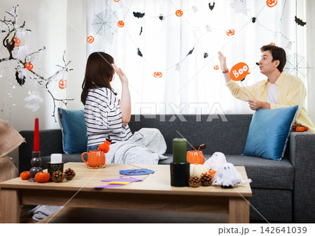 young couple having fun at home during halloween preparation. They enjoy the festive pumpkin garland and other decorations for a spooky party. young couple having fun at home during halloween preparation. They enjoy the festive pumpkin garland and other decorations for a spooky party. 142641039