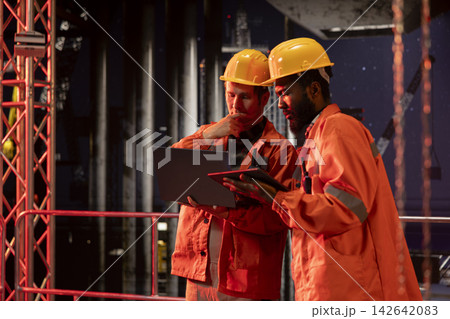 Industrial engineers inspect offshore drilling rig systems using gadgets to monitor emissions while extracting natural gas and petroleum. Ensuring efficient oil production for the industry. Industrial engineers inspect offshore drilling rig systems using gadgets to monitor emissions while extracting natural gas and petroleum. Ensuring efficient oil production for the industry. 142642083
