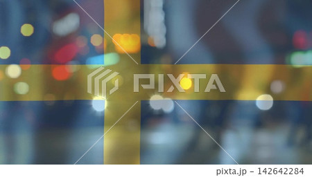 Displaying Swedish flag over blurred night street, showing bokeh, headlights, pedestrians in coats 142642284