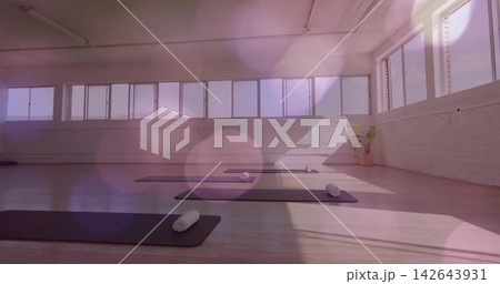 Displaying front yoga mat featuring rolled white towel on wooden floor in studio by long windows 142643931