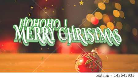Displaying centered 3D holiday text dominating on wooden tabletop, with red glass ornament nearby 142643933