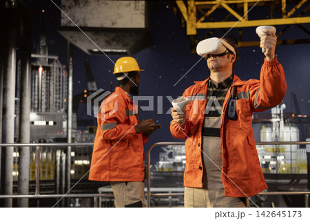 Industrial male employee on offshore platform wears virtual reality gear to oversee oil and gas drilling simulation, using augmented technology for advanced modern rig maintenance. 142645173