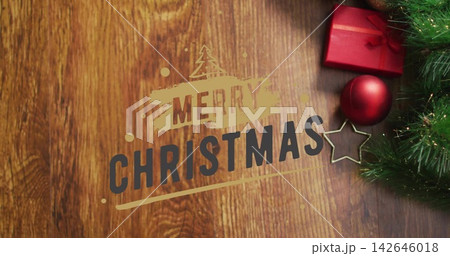 Displaying MERRY CHRISTMAS text on wood tabletop, showing red box and bauble, gold star, pine sprig 142646018
