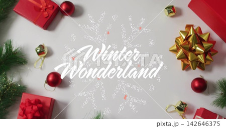 Surrounding centered white Winter Wonderland with dotted snowflake on table, red boxes, gold bow 142646375