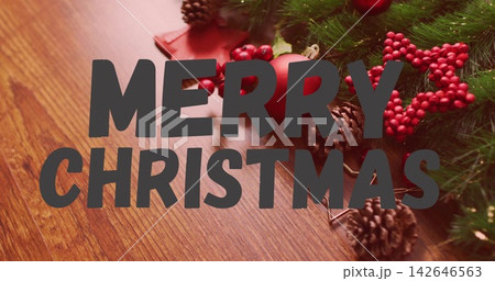 Displaying large gray MERRY CHRISTMAS text over wooden table, with pine cones and red ornament Displaying large gray MERRY CHRISTMAS text over wooden table, with pine cones and red ornament 142646563