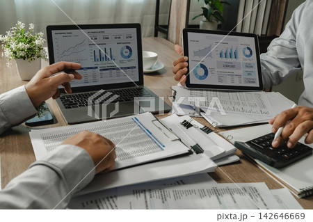 Two businessmen analyzing financial dashboards during business meeting with spreadsheet reports and calculator on laptop and tablet for data analysis and performance review. Two businessmen analyzing financial dashboards during business meeting with spreadsheet reports and calculator on laptop and tablet for data analysis and performance review. 142646669
