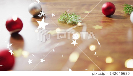 Styling tabletop with red baubles, fairy lights, fir sprigs, gold stars on wooden surface 142646689