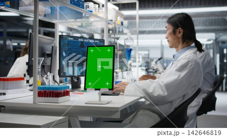 Lab expert at desk using green screen tablet, looking at molecular model, doing research tasks. Asian man using bioengineering program on mockup device in medical lab, camera A 142646819