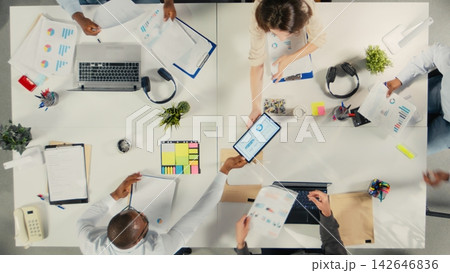 Top down view of associates meeting to review budgeting and resource allocation in a briefing session. Multinational company work team analyzes data for strategic planning. Top down view of associates meeting to review budgeting and resource allocation in a briefing session. Multinational company work team analyzes data for strategic planning. 142646836
