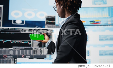 Manager using isolated screen smartphone to compare company metrics on digital videowall before making decisions. Entrepreneur analyzing key performance indicators using mockup phone, camera A 142646921