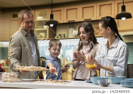 Pre-teen girl and little brother joining parents for pizza night in the kitchen, laughing as they add fresh ingredients and pepperoni to the dough. Cozy family cooking time with teamwork. Pre-teen girl and little brother joining parents for pizza night in the kitchen, laughing as they add fresh ingredients and pepperoni to the dough. Cozy family cooking time with teamwork. 142646950