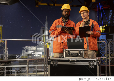 Diverse engineers colleagues using walkie talkie communication on marine oil platform, assessing fuel extraction data to maintain balance of natural gas and petroleum from the ocean habitat. 142647147