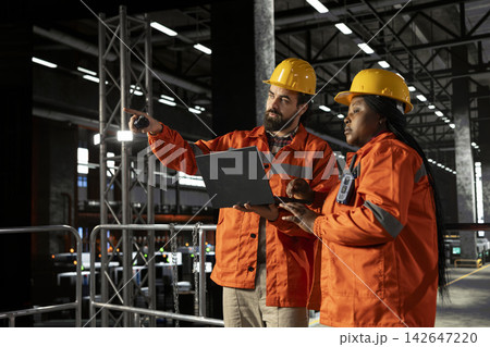 Diverse engineers team using walkie-talkie communication in large-scale factory, radio signal communication ensuring efficient machinery hall operations for production line and steel work. Diverse engineers team using walkie-talkie communication in large-scale factory, radio signal communication ensuring efficient machinery hall operations for production line and steel work. 142647220